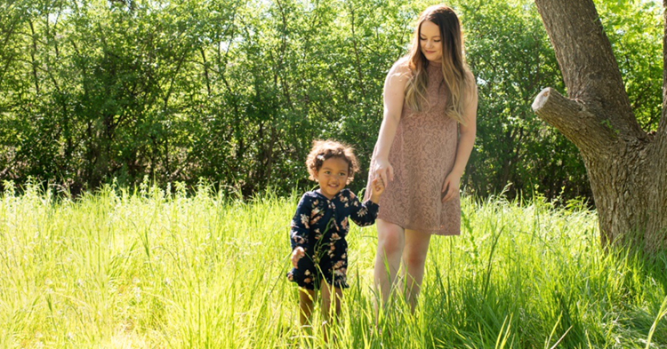 mom and daughter walking through a grass field