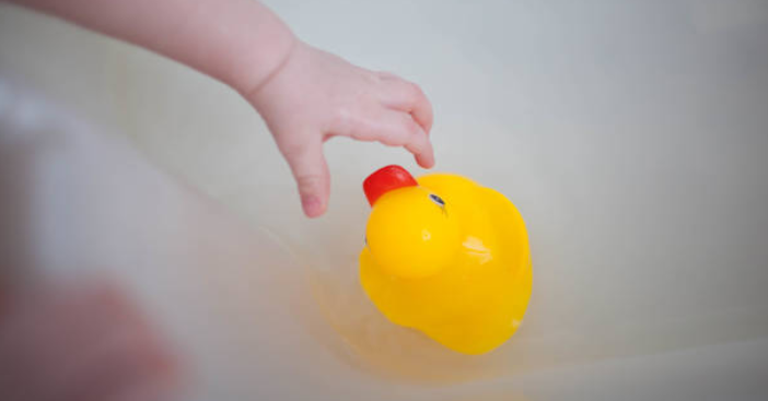 toddler hand reaching for rubber ducky in tub